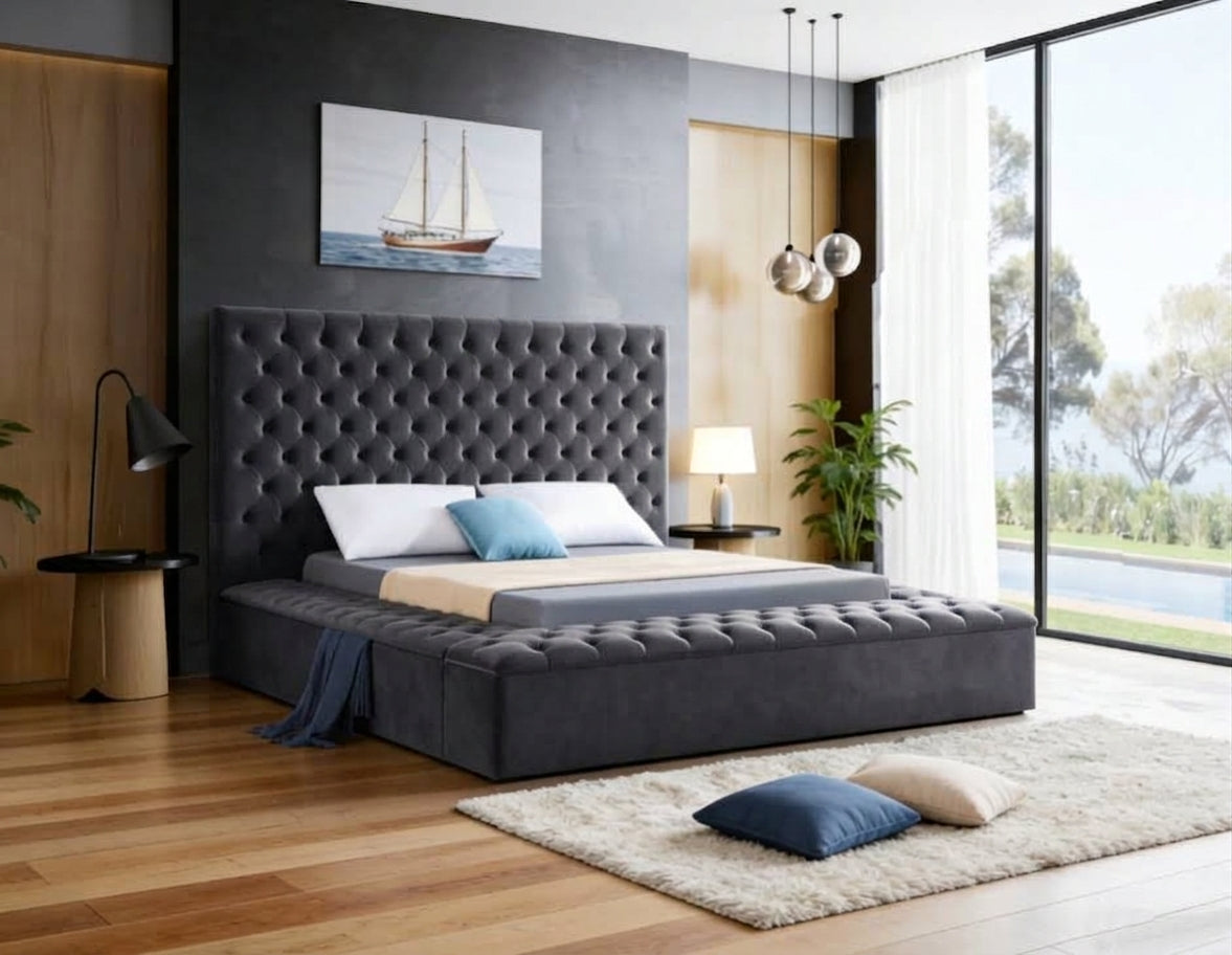 A modern bedroom featuring a dark gray tufted platform bed with a tall, button-tufted headboard. The bed is styled with white and blue pillows, a beige throw blanket, and a dark blue throw pillow.